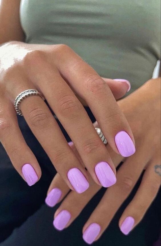 A hand showcasing short, neatly shaped square nails painted in a solid, vibrant pastel purple gel polish.