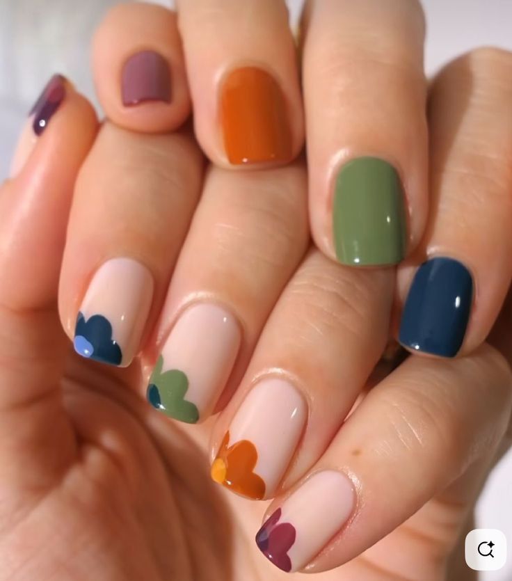 Short, square-shaped nails featuring a "skittle" style mix of solid earthy tones like sage green, terracotta, and deep teal, paired with abstract, wavy flower-like shapes in matching colors on a sheer nude base.