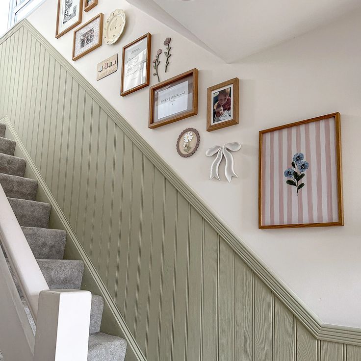 A staircase wall featuring vertical paneling decorated with an arrangement of small, light-framed art prints.