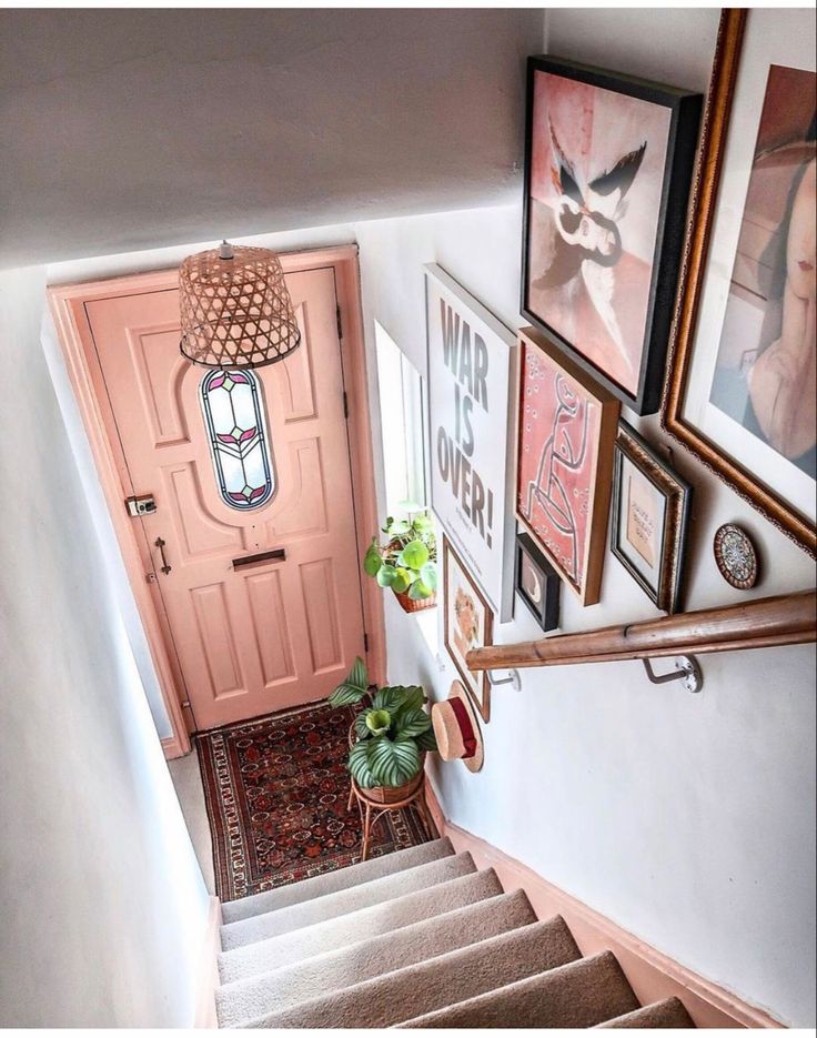 A colorful, eclectic staircase landing featuring a pink door and a gallery wall filled with assorted framed art and decor.