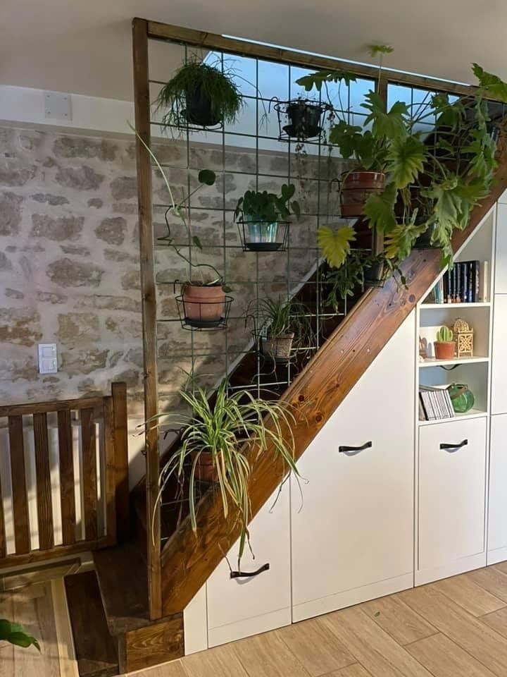 A staircase featuring a metal grid trellis covered in various potted plants, paired with white built-in storage cabinets installed beneath the stair slope.