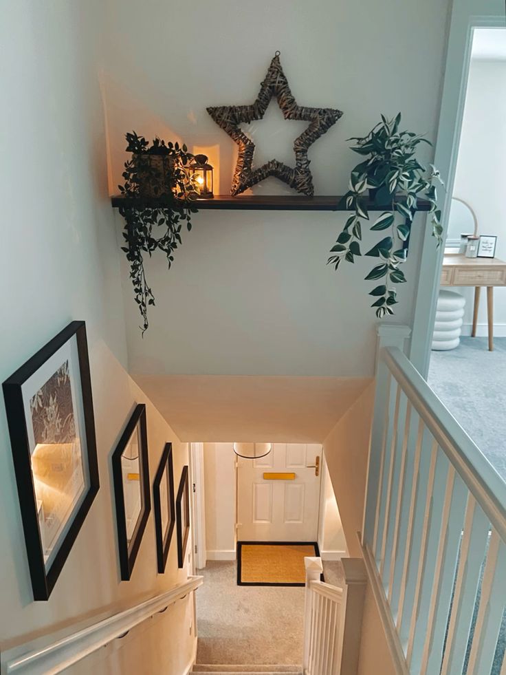  A staircase landing featuring a wooden floating shelf styled with greenery, a star-shaped decorative item, and warm lighting, with black-framed art prints hung on the adjacent wall