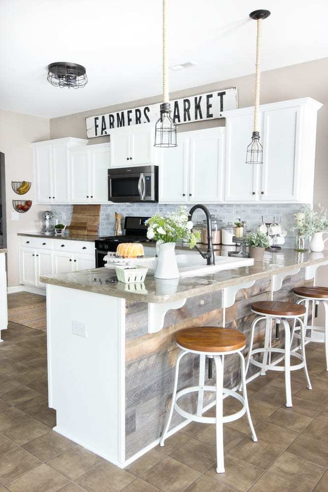 White kitchen cabinets with a long, weathered wood "FARMERS MARKET" sign sitting across the top ledge.