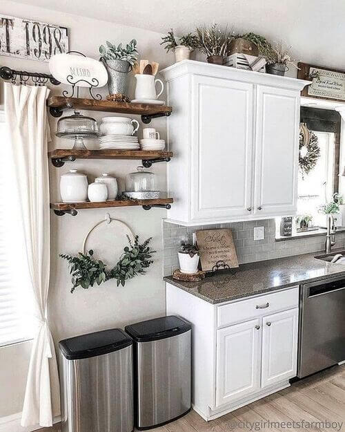 White upper cabinets and dark wood open shelves decorated with small potted plants, white ceramic dishes, and a small white wooden crate.