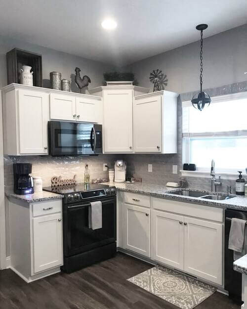 White kitchen cabinets with farmhouse decor on top including a wooden crate, metal canisters, a black rooster figurine, and a small metal windmill.