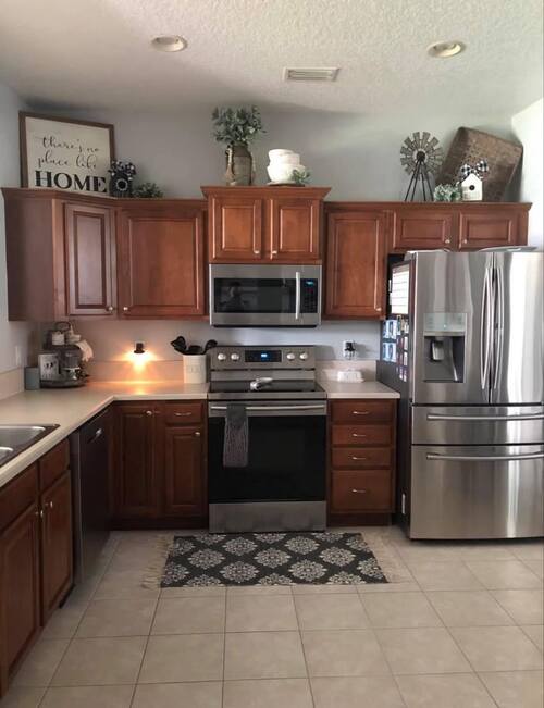 Stained wood kitchen cabinets with home decor items on top, including a framed quote sign, a ceramic jug with greenery, and a small metal windmill.