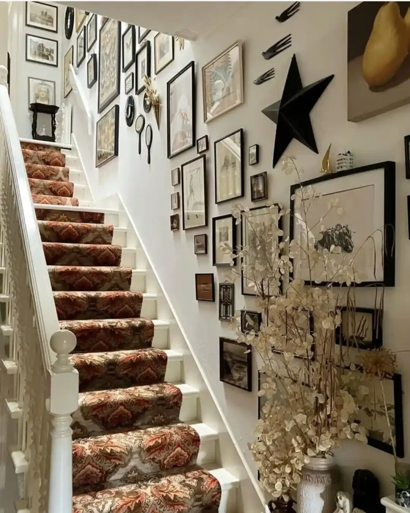 A maximalist staircase gallery wall packed with black-framed eclectic art prints and vintage hand mirrors, paired with a patterned orange and brown staircase runner on white stairs.