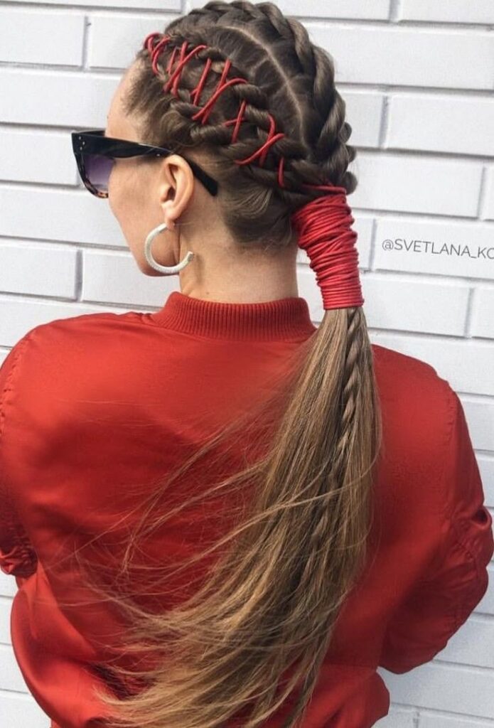 Woman from behind with light brown hair in thick side braids laced with red cord, ending in a low ponytail wrapped in red cord, showing an edgy prom hairstyle.