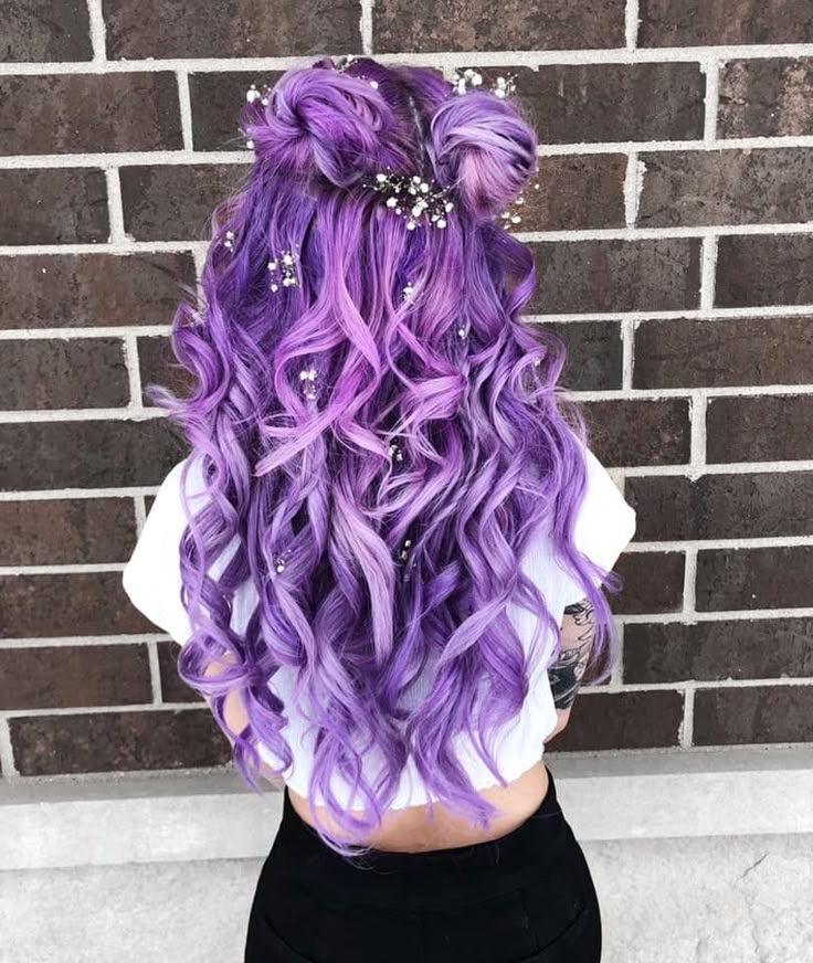 A back view of a whimsigoth prom hair look featuring curly lavender hair in a half up space bun style with tiny flower pins.