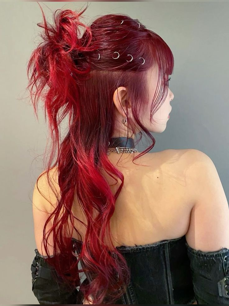 Side view of a woman with bright red hair in a messy half-up bun accented with silver hair rings, showcasing a grunge prom hair look.