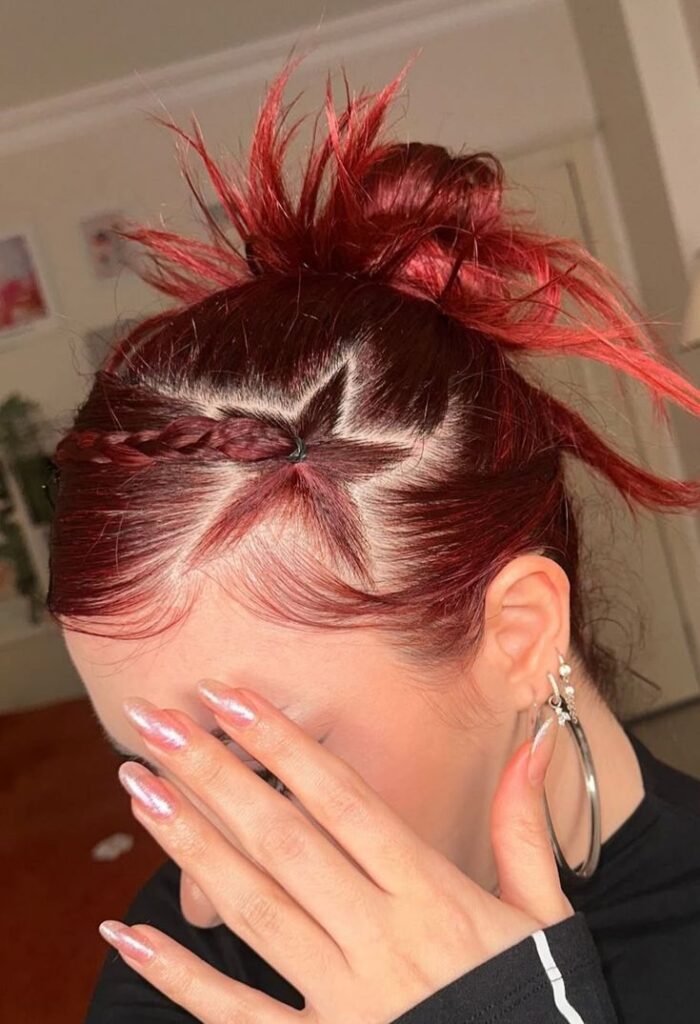 A close-up of a vibrant red Y2K prom hairstyle featuring a sharp star-shaped hair parting and a spiked messy bun.