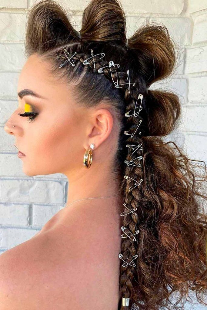 A side profile of an edgy prom hairstyle featuring a thick braid decorated with numerous silver safety pins.
