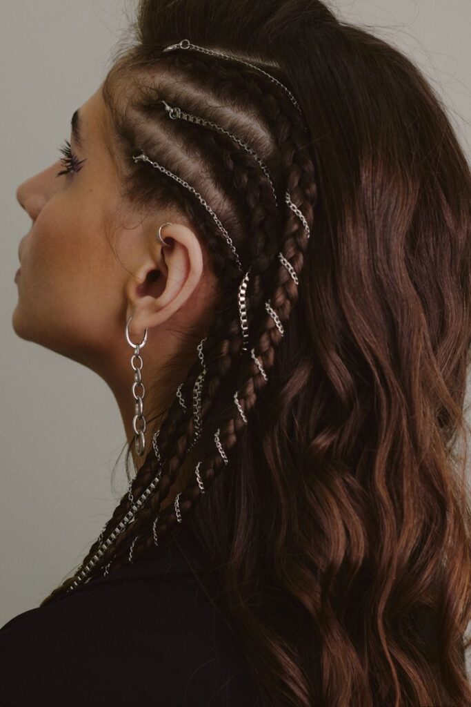 Profile view of an alt prom hairstyle with brunette waves and side braids interlaced with silver metal chains.