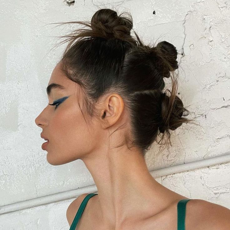 A profile view of a woman with her hair pulled back into three small, messy knots creating an alt prom hairstyle up do.