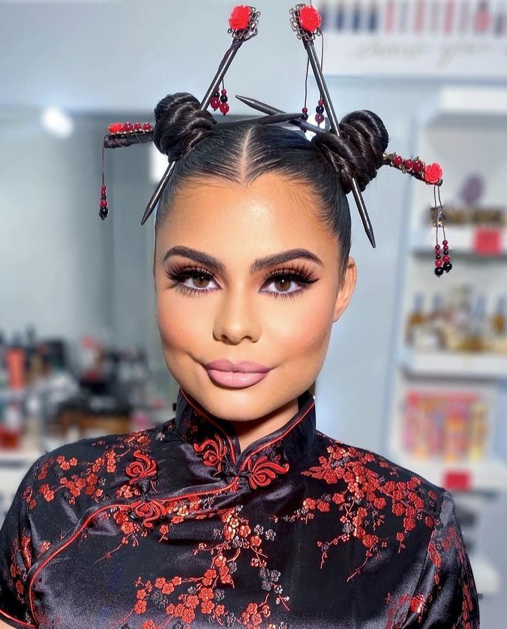 A woman with an edgy prom hairstyle featuring sleek space buns, red floral hair accessories, and a black and red floral high-neck outfit.