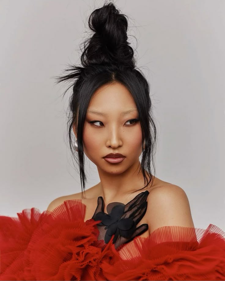 A woman with a Y2K prom hair up do featuring a high, textured bun, sleek face-framing pieces, and bleached eyebrows.