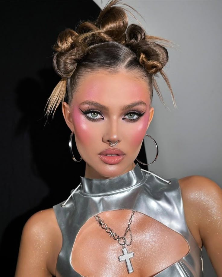 A woman with green eyes wearing a silver metallic top and a cross necklace, sporting a Y2K prom hairstyle with three sleek space buns and spiked ends.