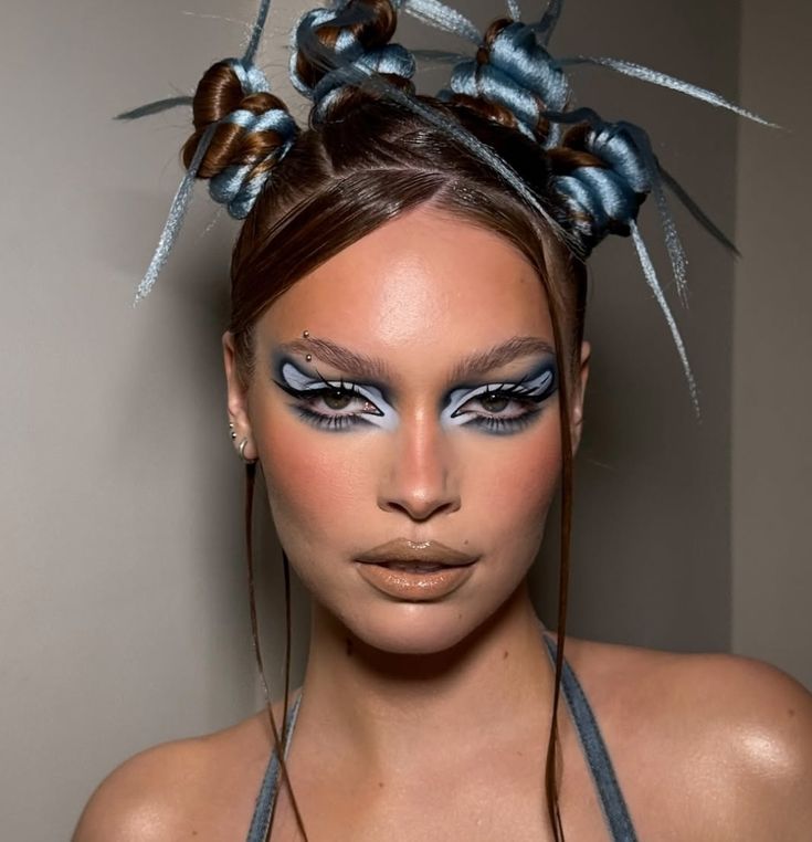 A woman with an alternative prom hairstyle featuring brown and icy blue braided buns with spiked ends and graphic blue eyeliner.