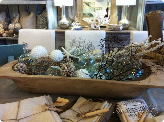 A large wooden dough bowl filled with transparent green glass fishing floats, dried sea fans, white starfish, and textured balls.