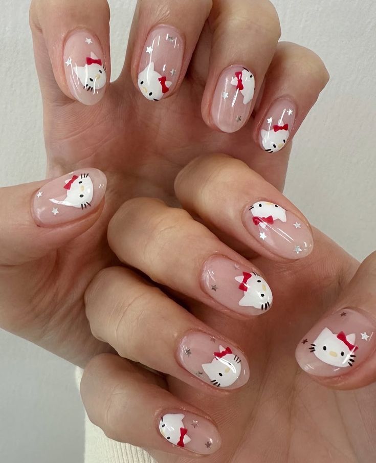 Almond-shaped nails with a sheer pink base coat, featuring small hand-painted Hello Kitty faces and tiny silver glitter stars on each finger.