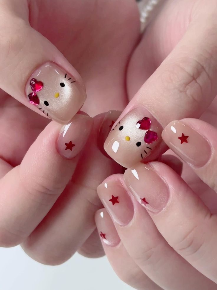 Short square-oval nails with a shimmering champagne cat-eye base and nude accent nails, featuring a Hello Kitty face with 3D ruby-red rhinestone heart bows and tiny red stars.