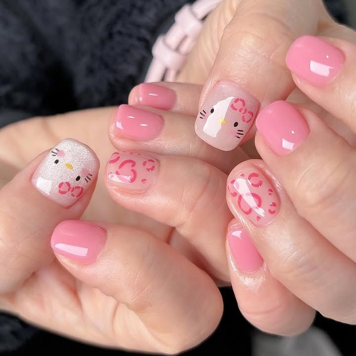 Short round nails featuring solid bubblegum pink polish, a Hello Kitty face over silver glitter, and sheer pink accent nails with a bright pink leopard print pattern.