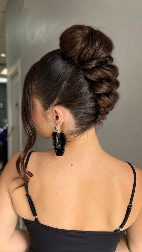 A back view of a woman with dark brown hair styled in an elegant French twist that leads up into a large, smooth top bun with several face-framing curls.