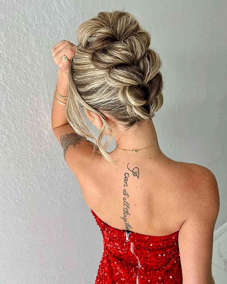 A back view of a woman with highlighted blonde hair in a highly textured, tiered updo consisting of multiple horizontal hair folds and a soft, loose fringe.