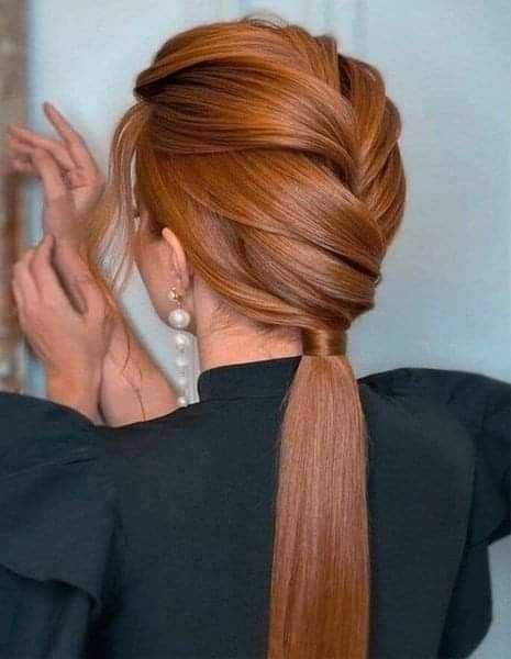 A back view of a woman with long ginger hair styled with thick, overlapping diagonal sections that transition into a smooth, low ponytail wrapped at the base.