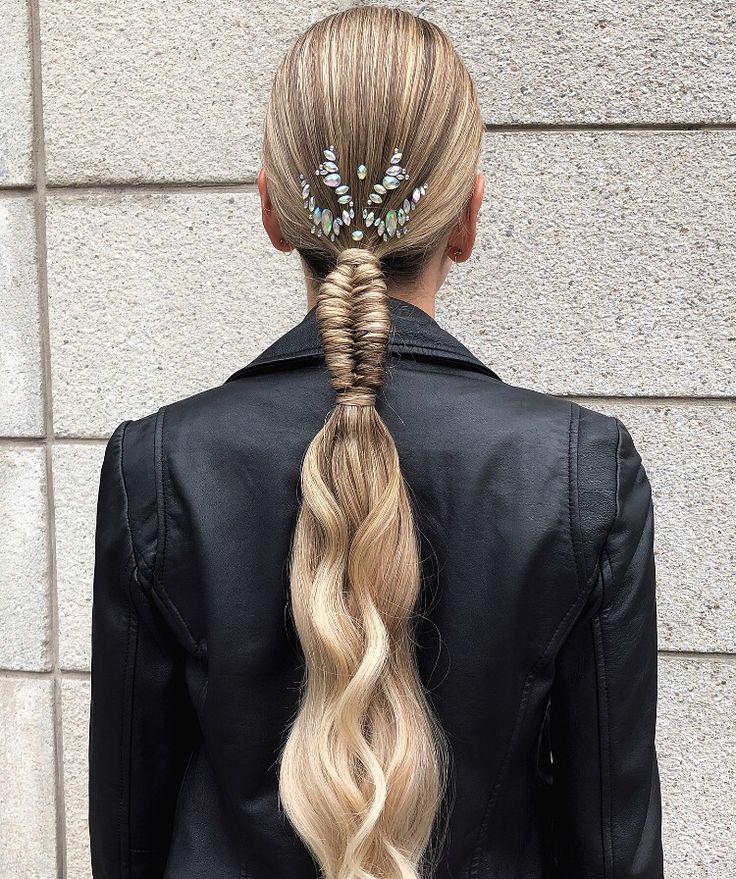 A back view of a person with blonde hair in a tight, sleek ponytail featuring a section of tight fishtail braiding at the base and crystal embellishments on the crown.