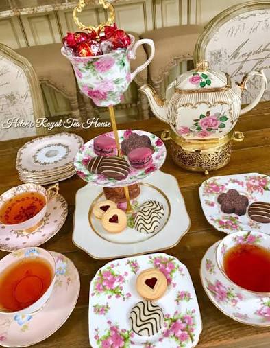 A tiered dessert stand topped with a floral teacup filled with red-wrapped chocolates, surrounded by heart-shaped cookies and macarons.