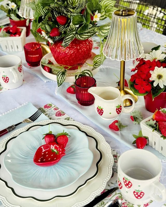 A beautifully set brunch table featuring light blue scalloped plates, small red strawberry-shaped bowls, and mugs decorated with little strawberries.