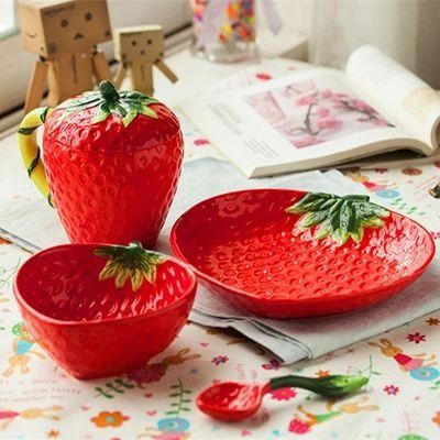 A collection of bright red ceramic kitchenware, including a lidded strawberry jar, a large berry-textured plate, a small bowl, and a matching spoon.