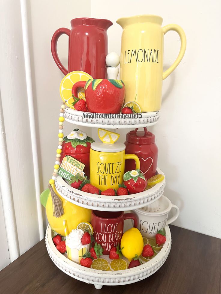 A white three-tiered beaded tray decorated with yellow "Lemonade" and red "I Love You Berry Much" pitchers, strawberry mugs, and faux fruit slices.