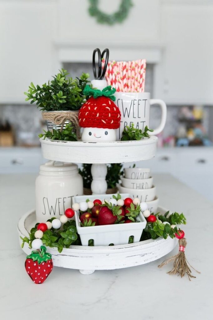 A white farmhouse tiered tray decorated with bright red strawberry decor and greenery.