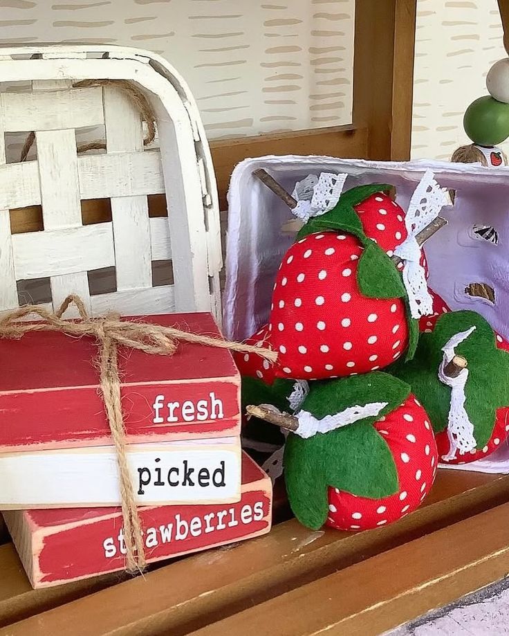 Close-up of plush red and white polka dot fabric strawberries in a white carton next to wooden blocks painted to look like books that read "fresh picked strawberries."