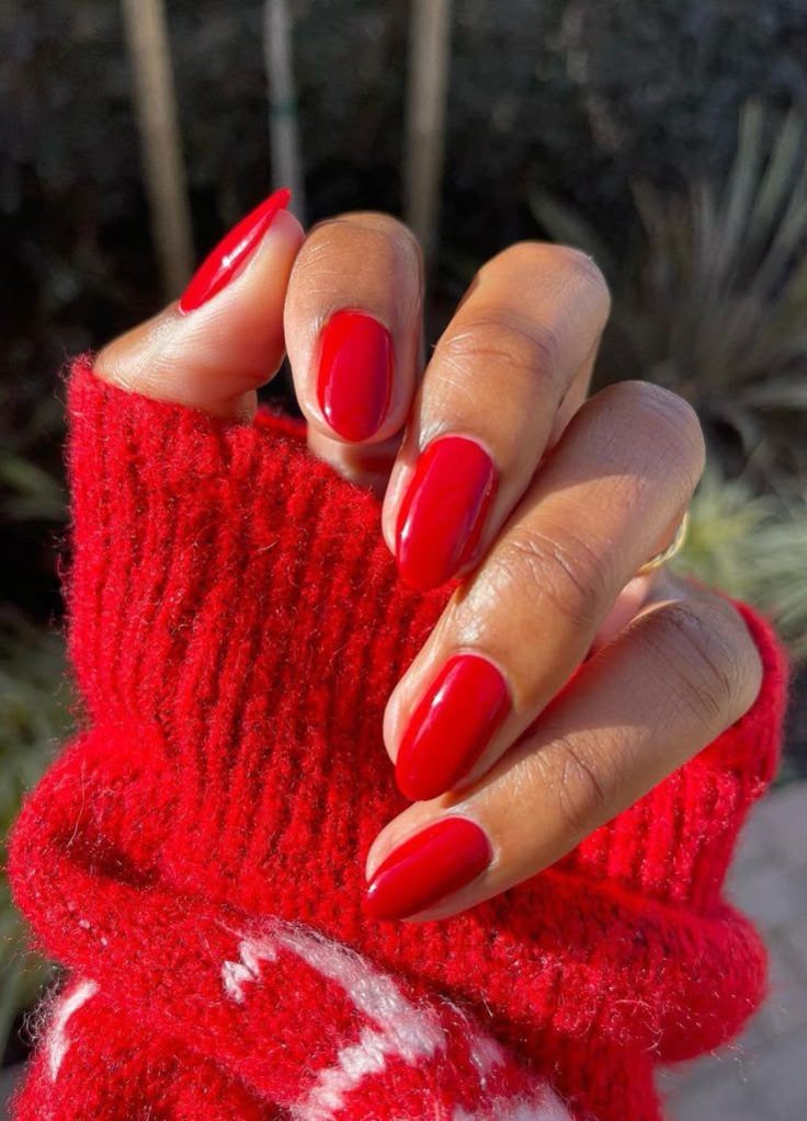 A hand with short, glossy red oval nails tucked into the sleeve of a chunky red and white knit sweater.