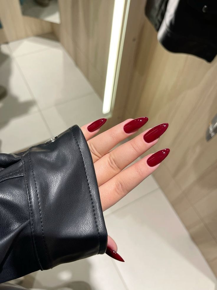 A hand with long, glossy deep maroon almond-shaped nails resting against the sleeve of a black leather jacket.