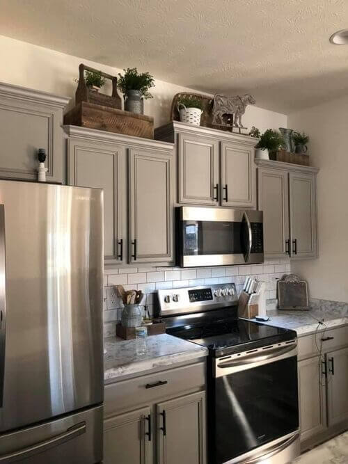 Staggered gray kitchen cabinets topped with rustic wooden boxes, green plants in metal containers, and a metal cow silhouette figure.
