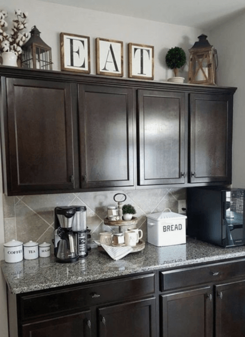 Dark wood kitchen cabinets decorated on top with large square wood block letters spelling EAT and two rustic wooden lanterns.