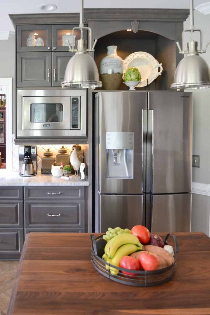 Large ceramic vases and a decorative plate provide above the fridge storage in a built-in gray cabinet nook. It is a clean example of above the fridge organization.