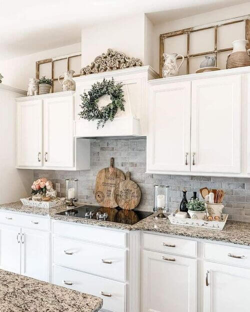 Corner view of white kitchen cabinets decorated with a wooden crate, a white jug, metal containers, a rooster figure, and a miniature windmill.