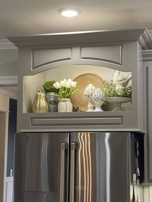 A lighted arched cabinet features white tulips and ceramic bird figurines. This elegant above the fridge decor creates a bright focal point.