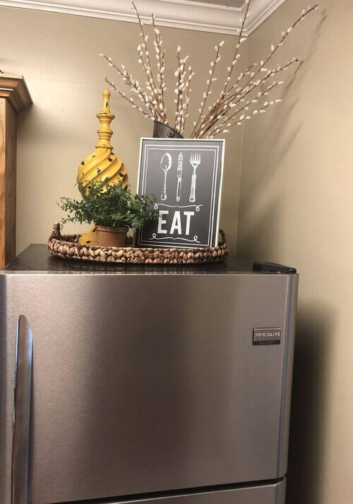 Vibrant top of the fridge decor farmhouse style featuring a woven tray. A chalkboard sign and greenery provide simple above the fridge ideas for a cozy kitchen.
