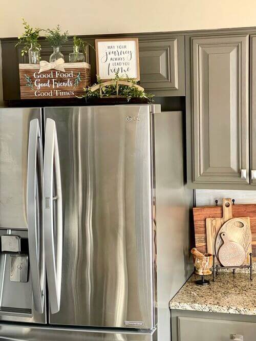 Rustic wooden signs and small glass herb vases create a top of the fridge decor farmhouse look. These are cozy above the fridge ideas for a homey kitchen.