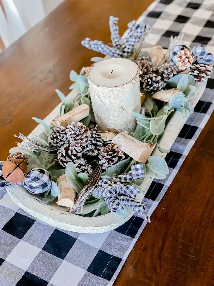 Whitewashed dough bowl with lamb's ear foliage, birch branch pieces, snowy pinecones, buffalo check accents, and a birch-textured candle.