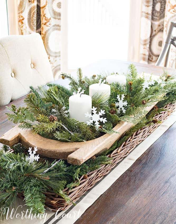 Wooden dough bowl centerpiece with an antique sled runner, fresh pine and cedar boughs, snowflake picks, and white pillar candles.