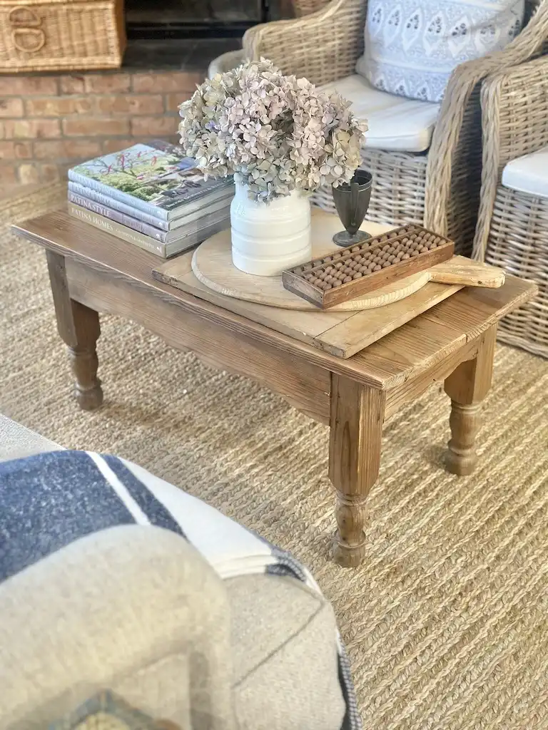 fall coffee table decor with taper candles in brass candlesticks, red mums in a white bowl and a pumpkin and books on the lower shelf