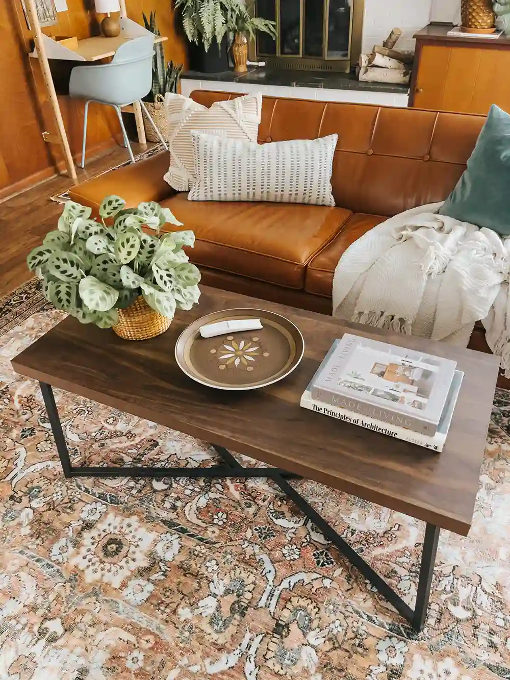 coffee table styling with a rattan tray holding a ceramic vase of white flowers and a candle, plus stacked books and brass candlesticks in a living room