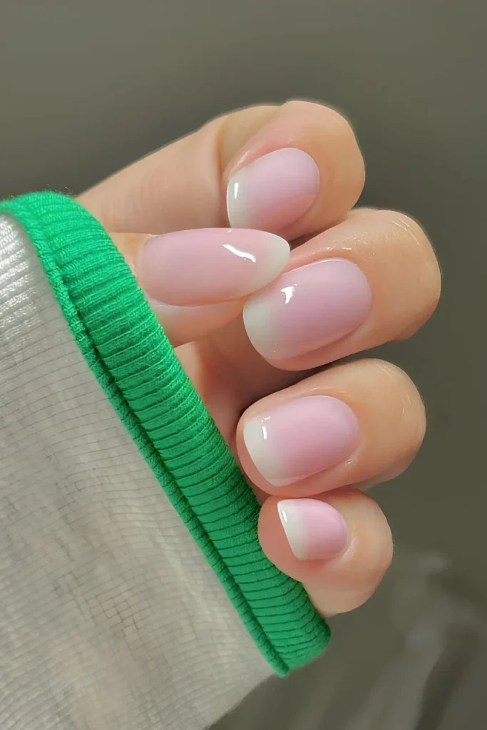 Short milky pink nails with gradient white French tips, short soft pink nails with an ombre French, short light pink nails, short almond and square nails, baby boomer nails, pink ombre French manicure, soft pink French tip nails, glossy gel nails, natural looking nails
